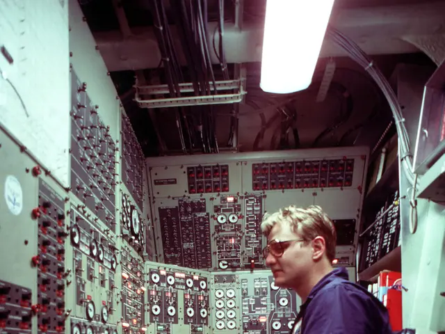 The image shows a man sitting at a desk in front of a control panel, illuminated by a light at the...