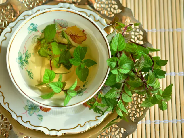 The image shows a cup of green tea with mint leaves on a silver tray placed on a table mat. The cup...