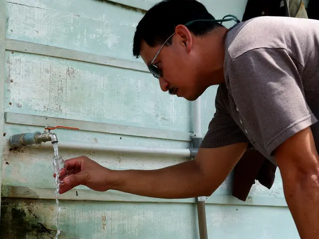 The image shows a man wearing goggles and drinking water from a tap attached to a wall. He is...