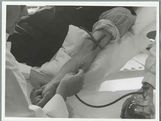 The image shows a black and white photo of a man laying in a hospital bed with a nurse standing...