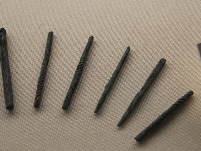 The image shows a group of five metal nails sitting on top of a table, with a board on the right...