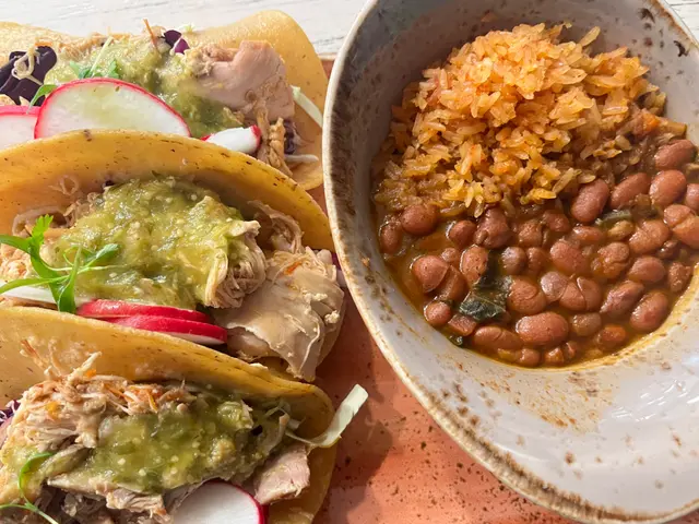 The image shows three tacos and a bowl of beans on a table. The tacos are filled with a variety of...