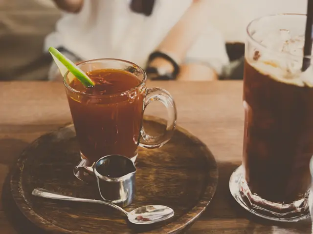 The image shows two glasses of iced tea on a wooden table, with a saucer and spoon beside them. In...