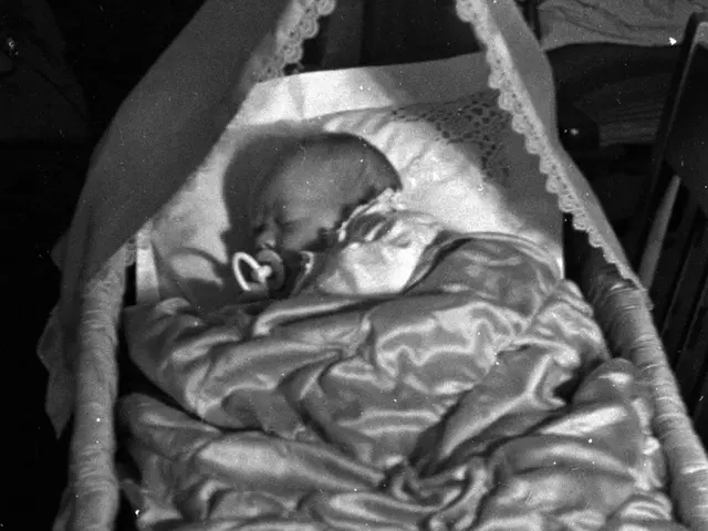 The image shows a black and white photo of a baby sleeping peacefully in a cradle, with a blanket...