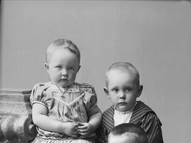 The image shows three children sitting on a bench in front of a wall. The image is in black and...