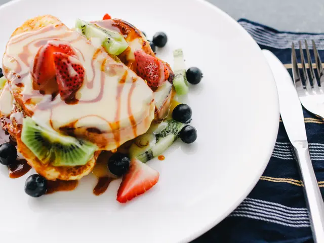 The image shows a white plate topped with pancakes covered in a variety of fruits, such as...