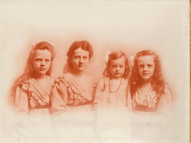 The image shows an old photo of four young girls posing for a picture. They are all smiling and...