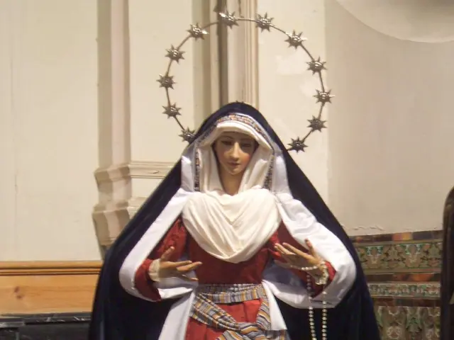 The image shows a statue of Our Lady of Fatima in a church, wearing a red and white dress and...