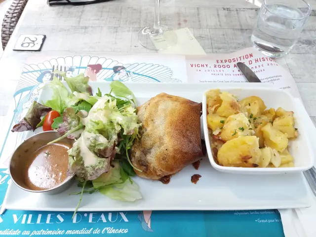 The image shows a table with a plate of food, a bowl of salad, a glass of water, a menu card, a...
