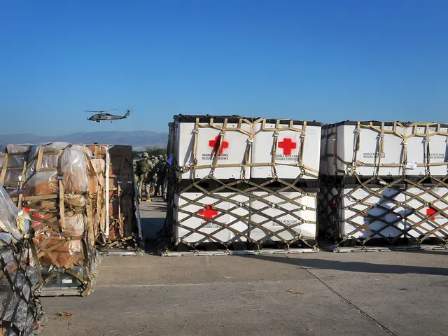 The image shows a group of people standing next to a large pile of boxes on the ground, with a...