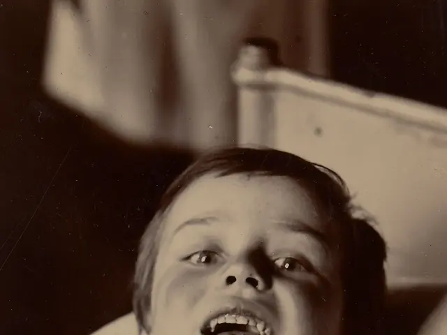 The image shows an old black and white photo of a young boy laying in a hospital bed with a cloth...