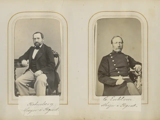 The image shows two men in military uniforms sitting next to each other. They are both wearing...