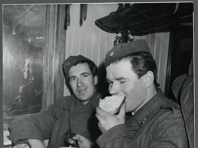 The image shows two men in military uniforms sitting on a train, eating food from a bowl. The image...