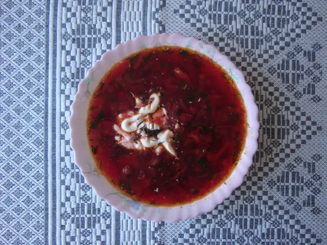 The image shows a bowl of borscht, a traditional Russian soup, placed on a table. The bowl is...