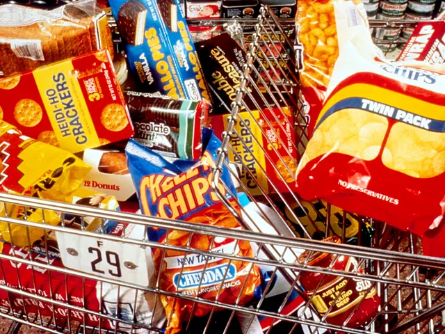 The image shows a shopping cart filled with a variety of snacks, including chips packets, bottles,...