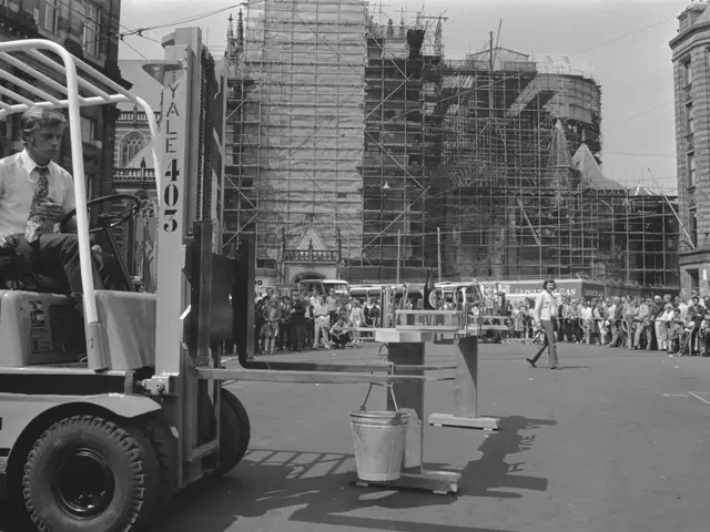 The image shows a man driving a forklift in front of a building under construction. He is wearing a...