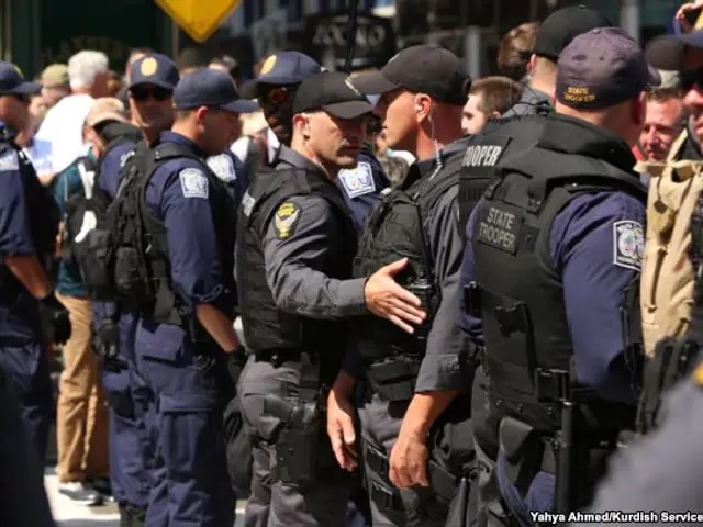 The image shows a group of police officers standing next to each other on a street. They are...