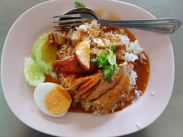 The image shows a white plate topped with a generous portion of nasi lemak, a traditional Malaysian...