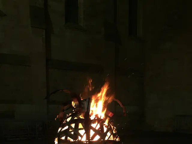 The image shows a person standing in front of a fire pit, holding a mobile phone in their hand. The...