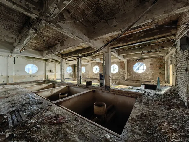 The image shows an abandoned building with a lot of windows, pillars, pipes, and other objects...