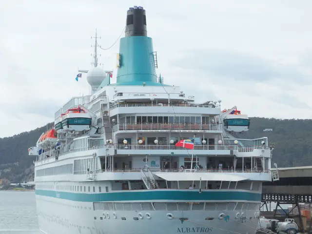 The image shows a large cruise ship docked at a dock with cars parked in front of it. On the right...