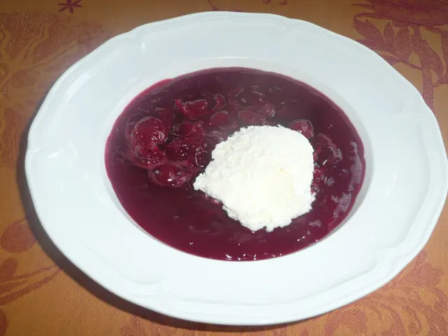 The image shows a white plate topped with a bowl of borscht, a traditional Russian dessert, and a...