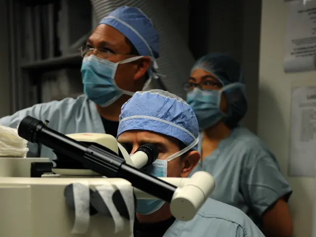 The image shows a group of surgeons wearing masks, caps, glasses, and gloves working on a patient...