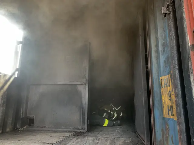 The image shows a firefighter in the doorway of a building with smoke billowing out of it, wearing...