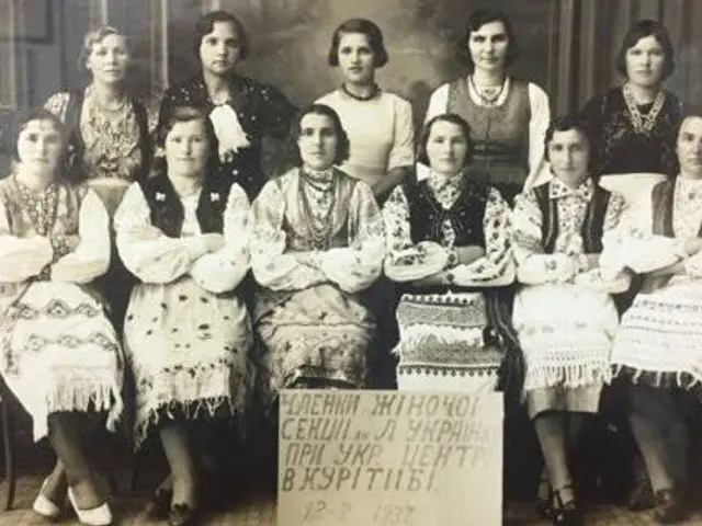 The image shows a group of women in traditional Ukrainian clothing posing for a photo in front of a...