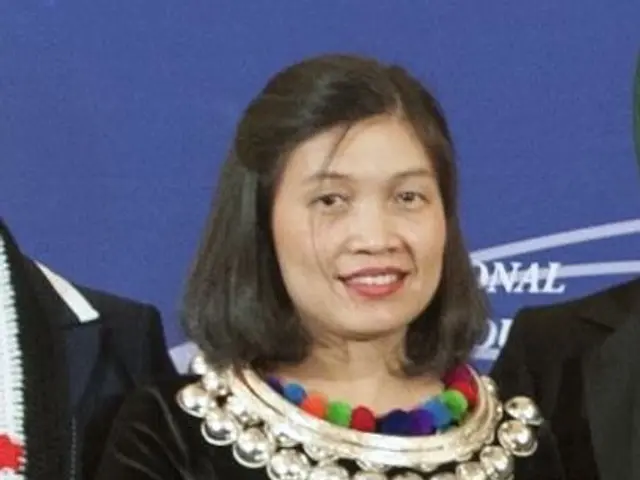 The image shows a woman in a black dress standing in the center, holding a trophy in her hands,...