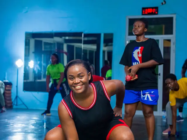 The image shows a group of people in a gym, with a woman in a squat position holding a pair of...
