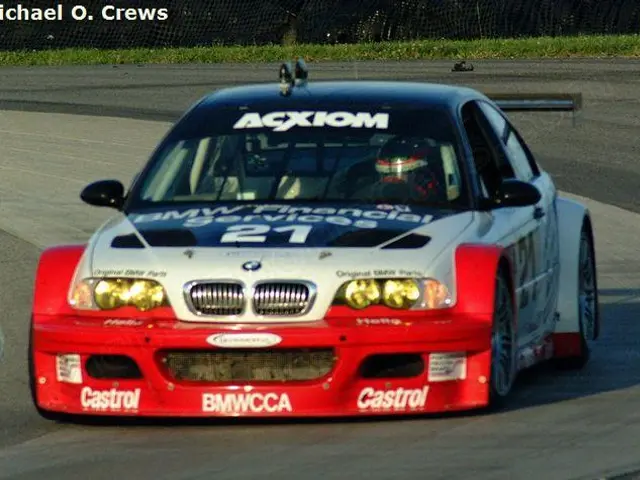 The image shows a person wearing a helmet and driving a BMW M3 GT3 on a race track. The car is...
