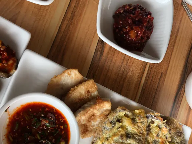 The image shows a wooden table topped with plates of food and bowls of dipping sauces, as well as...