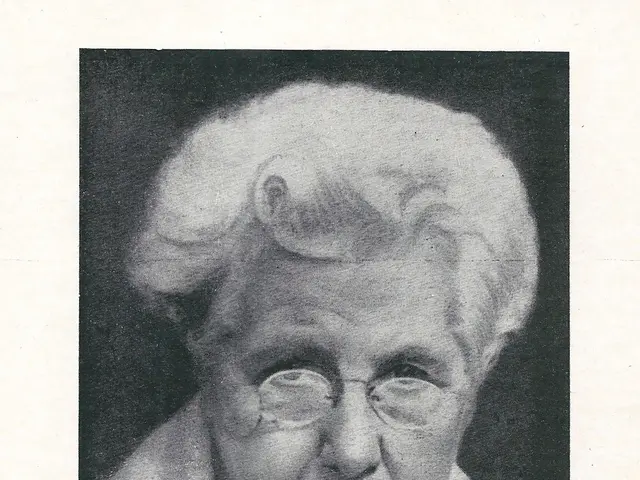 The image shows a black and white photo of an elderly woman wearing glasses. At the bottom of the...