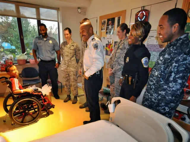 The image shows a group of people standing around a hospital bed, with a boy in a wheelchair in the...