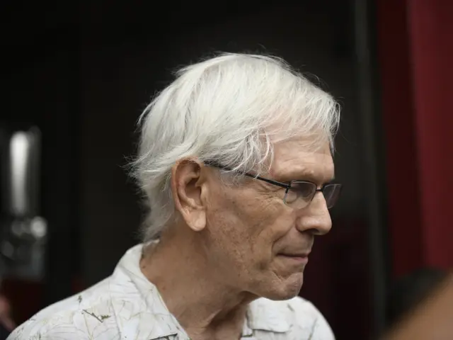 The image shows Bernie Ecclestone, CEO of the Formula One Group, wearing a white shirt and glasses....