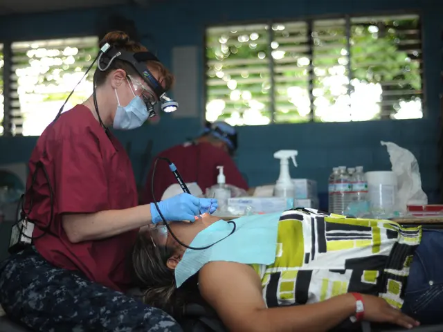 The image shows a woman laying on top of a bed next to a dentist wearing a mask, goggles, and...