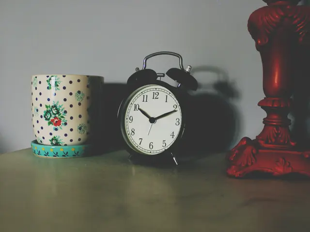 The image shows an alarm clock sitting on top of a table next to a cup, with a wall in the...