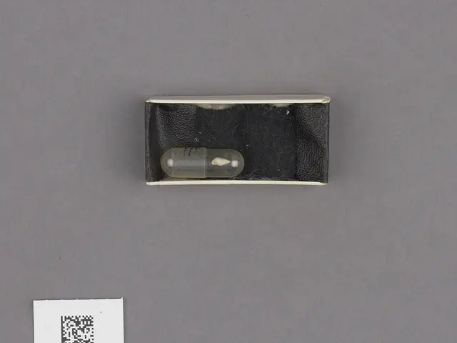 The image shows a black box with a small pill in it sitting on top of a table, accompanied by a...