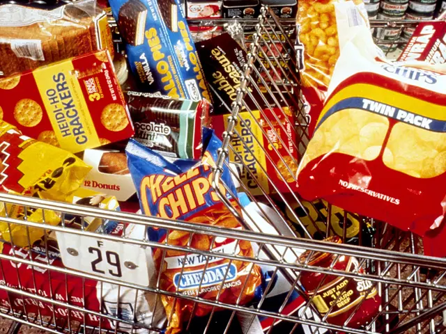 The image shows a shopping cart filled with a variety of snacks, including chips packets, bottles,...