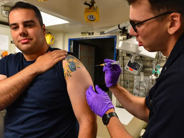 The image shows a man getting a vaccine from a doctor wearing a blue t-shirt and purple gloves. The...