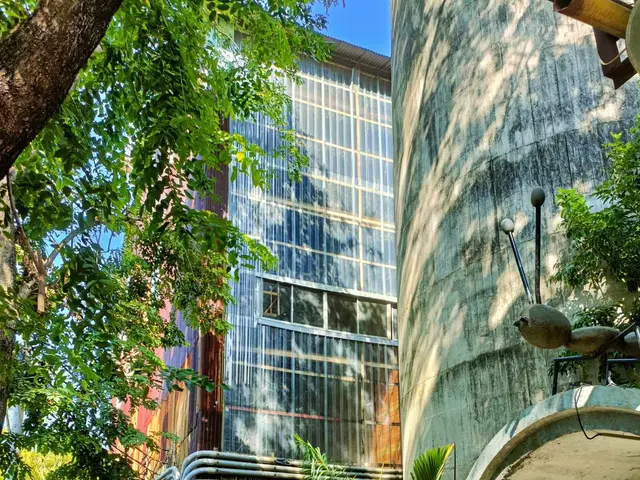 The image shows a courtyard with potted plants and trees in front of a building, surrounded by lush...