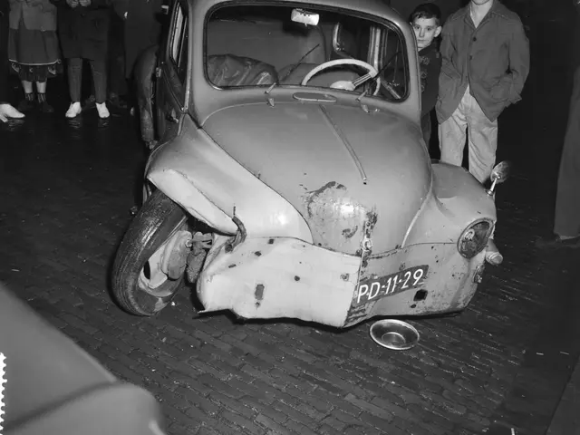 The image shows a black and white photo of a car that has been involved in a crash, with a group of...