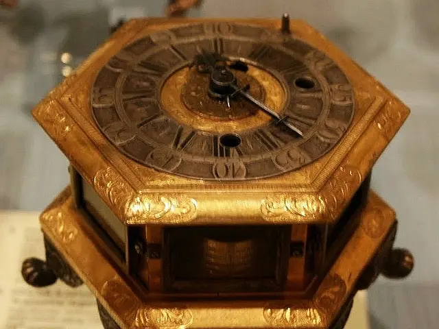 The image shows a small wooden clock sitting atop a table, with a paper beneath it and a blurred...