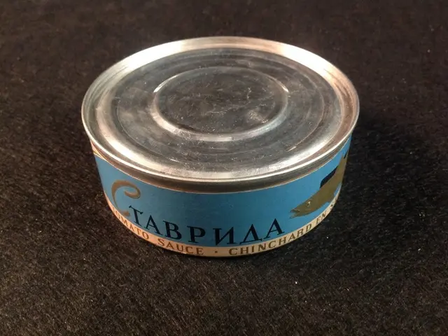 The image shows a can of tuna sitting on top of a black table. The can is silver in color and has a...
