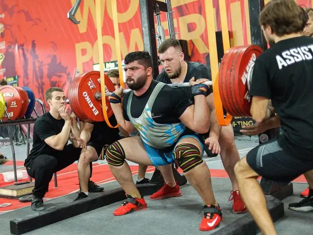 The image shows a group of men in a gym doing squats with barbells, surrounded by gym equipment and...