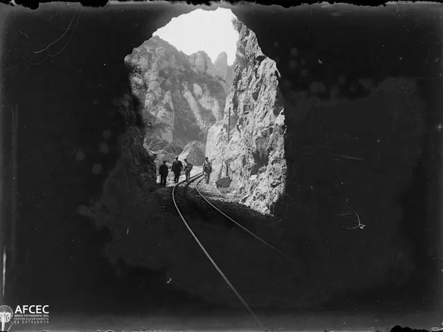 The image shows a black and white photo of a group of people walking through a tunnel, surrounded...