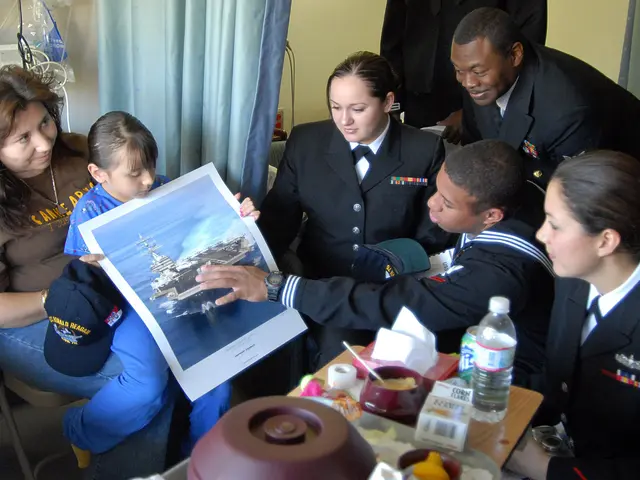 The image shows a group of people sitting around a table in a hospital room. On the table there are...