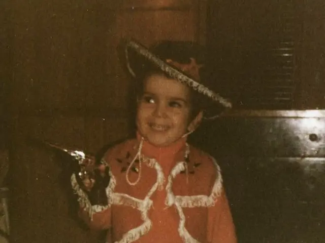 In this image, we can see a kid in front of the wall wearing clothes and hat. There is a window in...