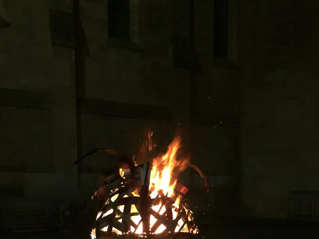 The image shows a person standing in front of a fire pit, holding a mobile phone in their hand. The...